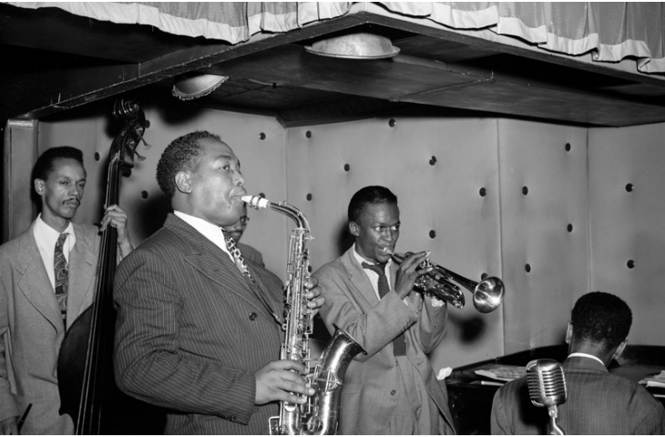 Miles Davis alongside Tommy Potter, Charlie Parker, Max Roach (partially hidden behind Parker) and Duke Jordan (from left to right), at Three Deuces, New York, 1947, William P. Gottlieb (through Wikimedia Commons)
